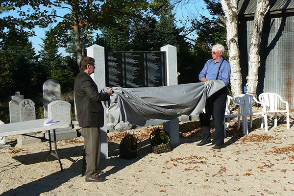 Bowman Mayor Michel David (right) and St. Paul's church member Stanley Cheslock unveil a monument honouring the 96 people buried on Cemetery Island.